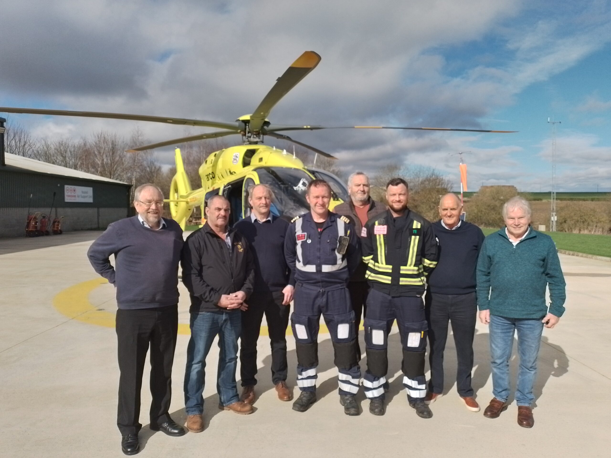 A group of people standing in front of a yellow helicopter